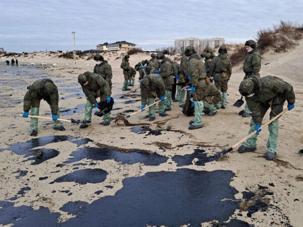 Люди убирают нефть с пляжа в защитной одежде и перчатках.