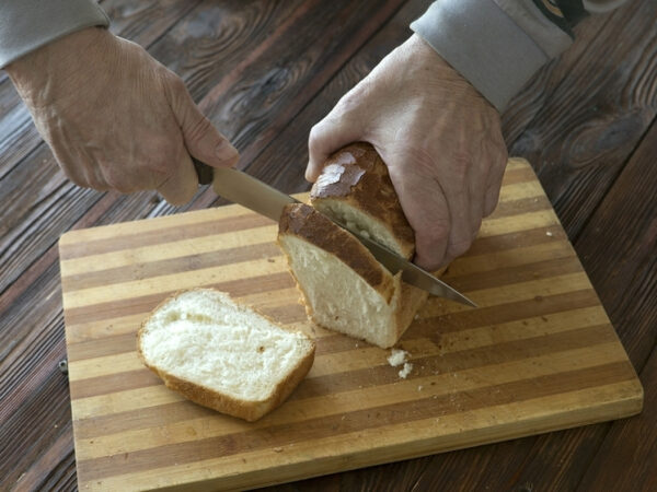 Руки режут свежий хлеб на деревянной доске.