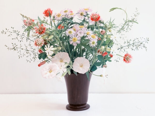 Букет полевых цветов в коричневой вазе на светлом фоне.
