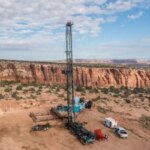 Буровая установка в пустыне на фоне скал и голубого неба.