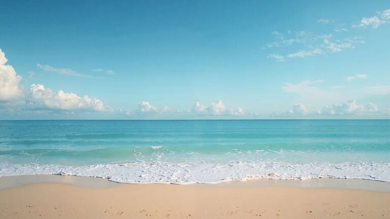 Песчаный пляж и спокойное голубое море с облачным небом на горизонте.