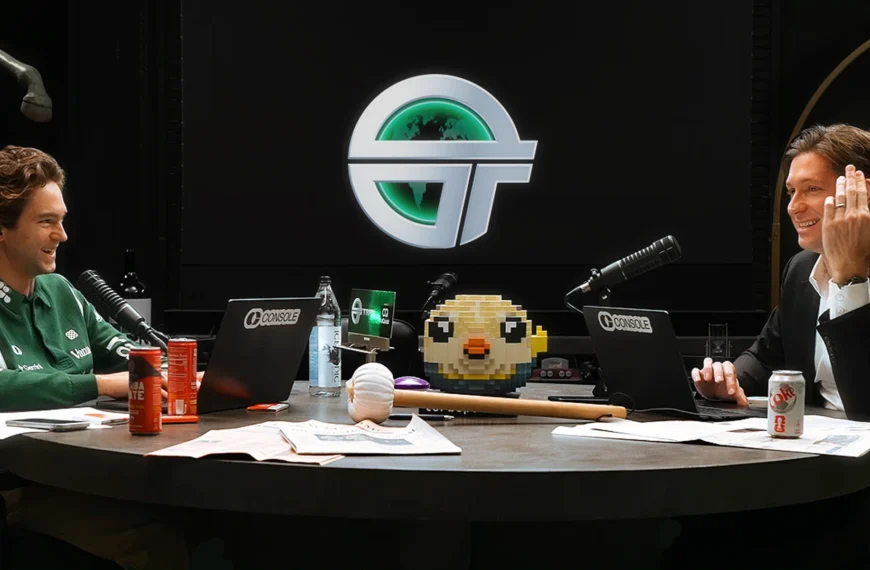 Двое мужчин за столом с ноутбуками и микрофонами, фон с логотипом.