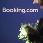Логотип Booking.com на синем фоне с цветами на переднем плане.