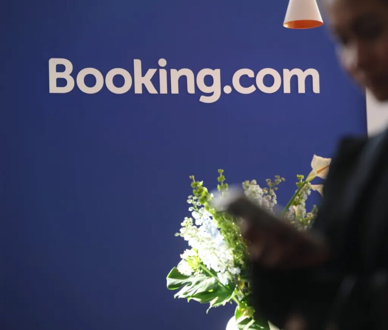Логотип Booking.com на синем фоне с цветами на переднем плане.