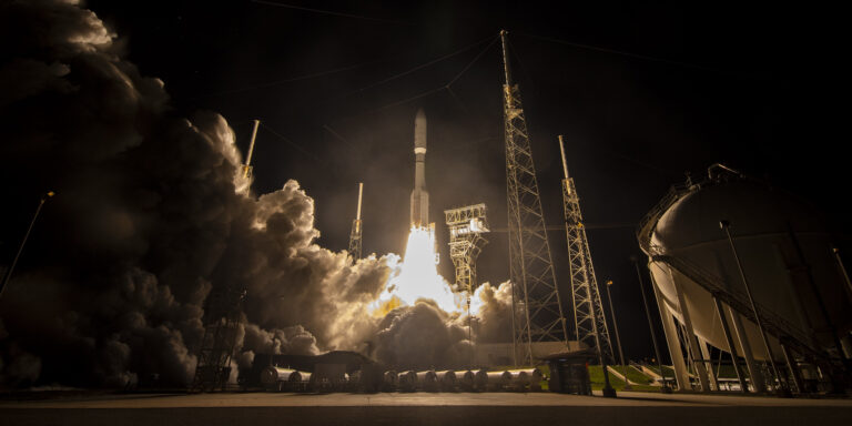 Запуск ракеты в ночи с космодрома, поднимается в небо, окружена дымом.