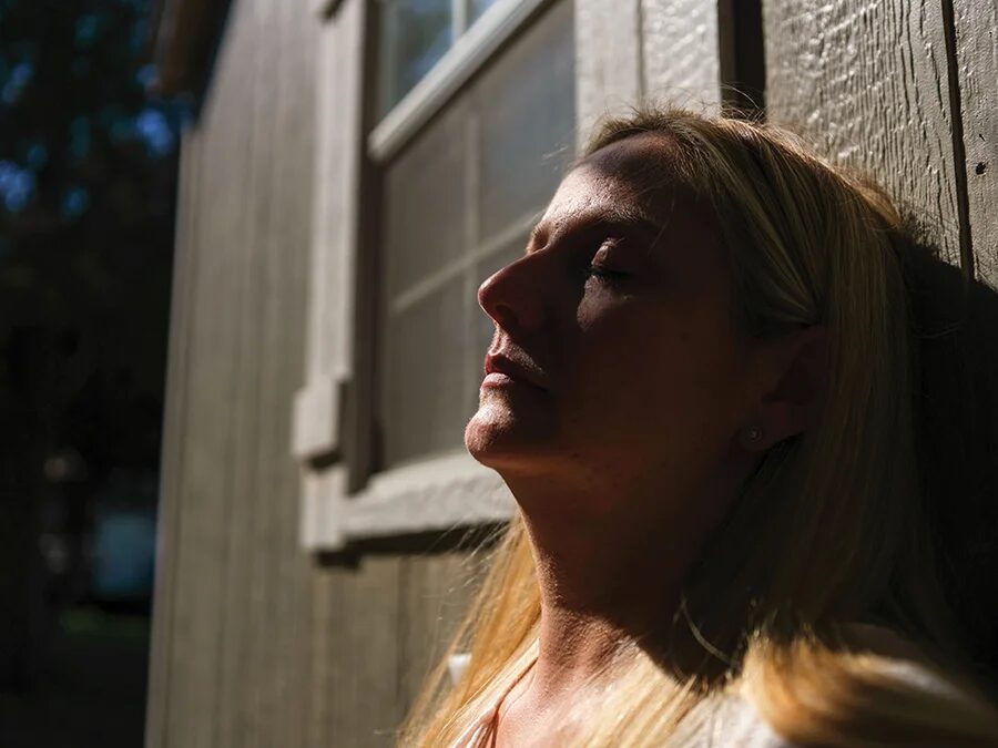 Женщина, прислонившаяся к зданию с закрытыми глазами