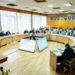 Заседание в конференц-зале с участием людей за круглым столом и экраном с презентацией.