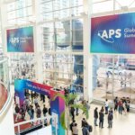 Конференция Global Physics Summit, люди в холле, баннер APS, большое остекление.