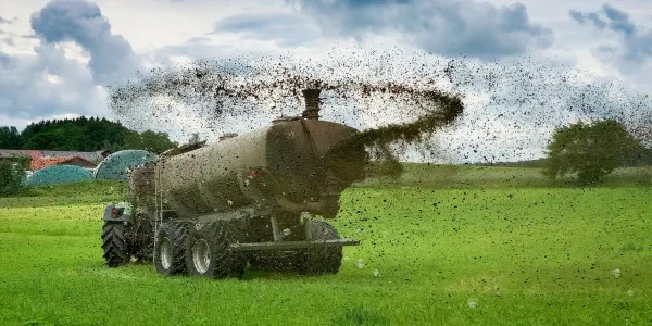 Трактор разбрасывает удобрения по полю.
