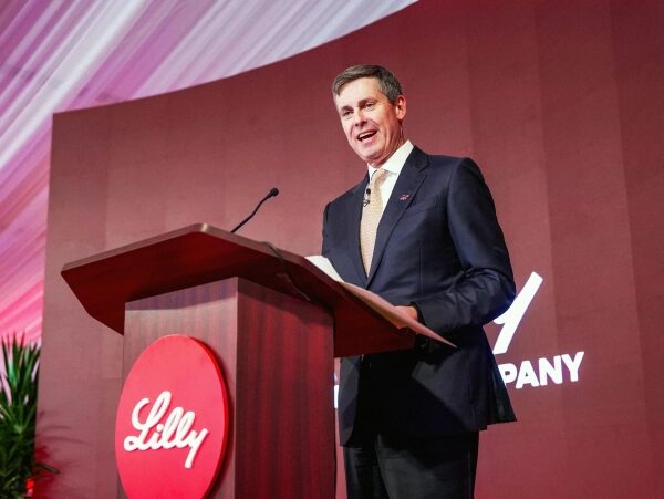 Мужчина выступает с речью на конференции Eli Lilly, красный фон.