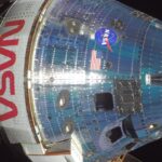 Космический корабль NASA с эмблемой и флагом США на фоне космоса.