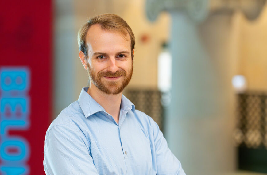 Мужчина в синей рубашке на фоне офисного интерьера, размытое лицо, бизнес-атмосфера.