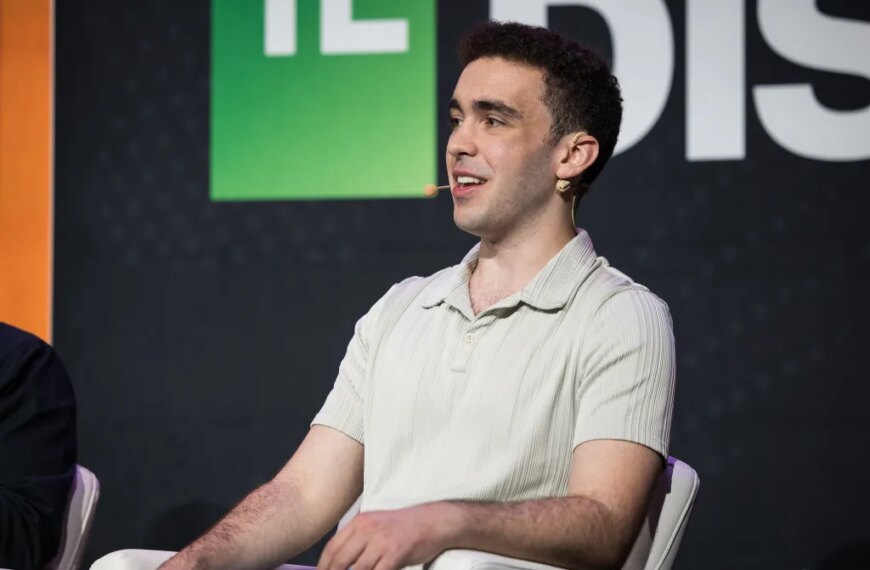 Человек на конференции TechCrunch Disrupt, сидит в светлой рубашке с микрофоном.