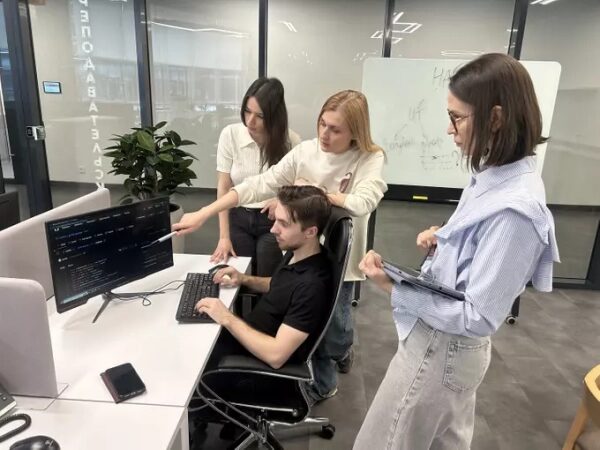 Команда программистов обсуждает код за компьютером в офисе. Работа над проектом.