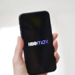 Смартфон с логотипом HBO Max в руке на светлом фоне.