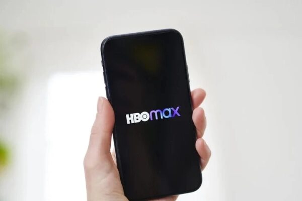 Смартфон с логотипом HBO Max в руке на светлом фоне.