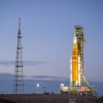 Ракета на стартовой площадке на рассвете, окружённая сигнальными башнями.