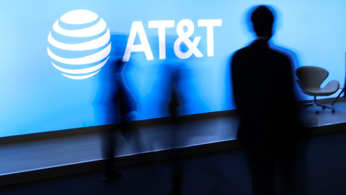 На конференции люди проходят мимо большого логотипа AT&T.