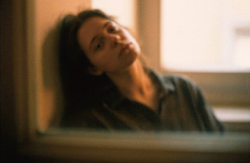 Человек у окна, расслабленная поза. Теплый тон изображения. Пастельная цветовая палитра.