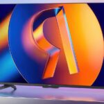 Телевизор на подставке с ярким цветным экраном на фиолетовом фоне.