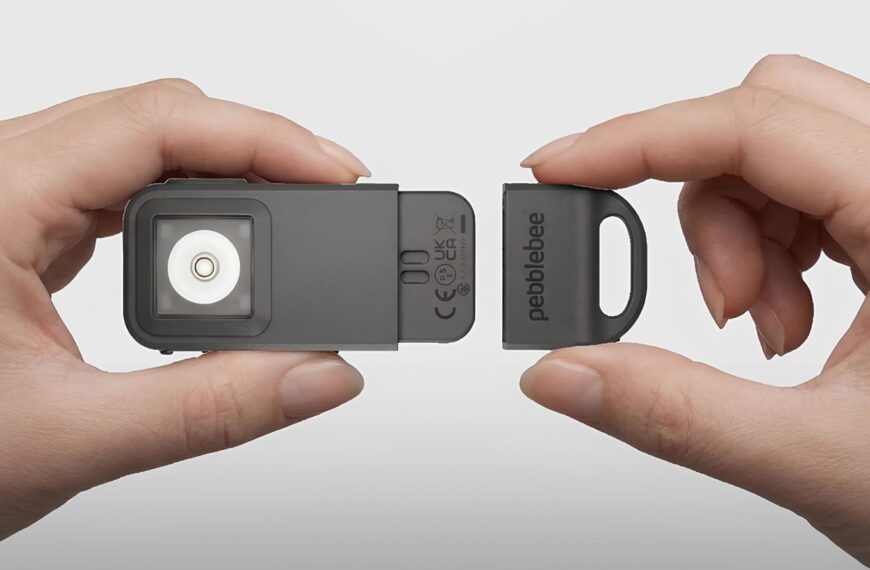 Руки держат устройство Pebblebee с открытым отсеком; серый корпус и белая внутренняя часть.