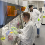 Учёные в лаборатории проводят исследования в защитных халатах и перчатках.