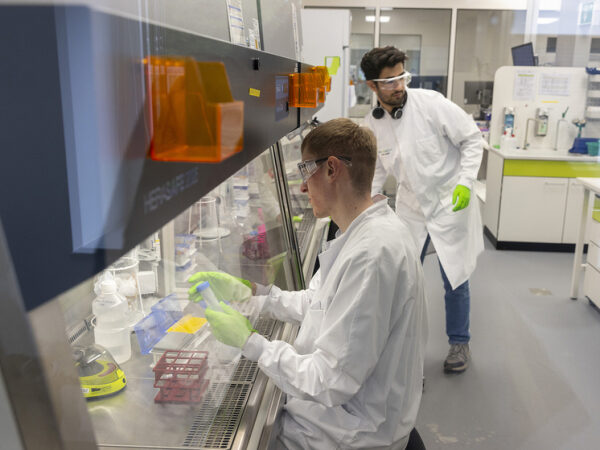 Учёные в лаборатории проводят исследования в защитных халатах и перчатках.