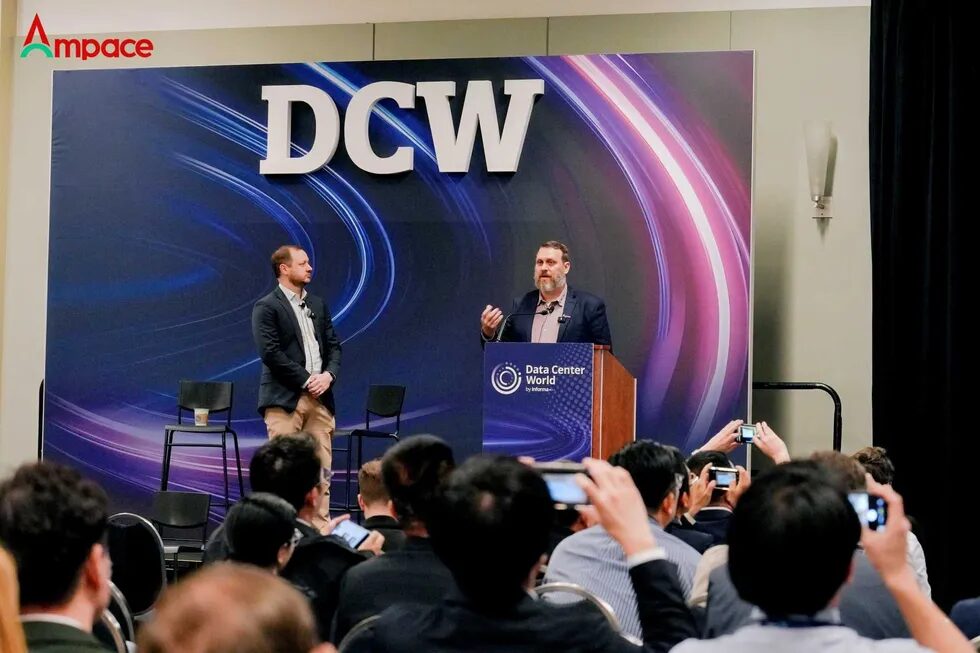 Выступление спикера на конференции DCW перед аудиторией с поднятыми телефонами на сцене.
