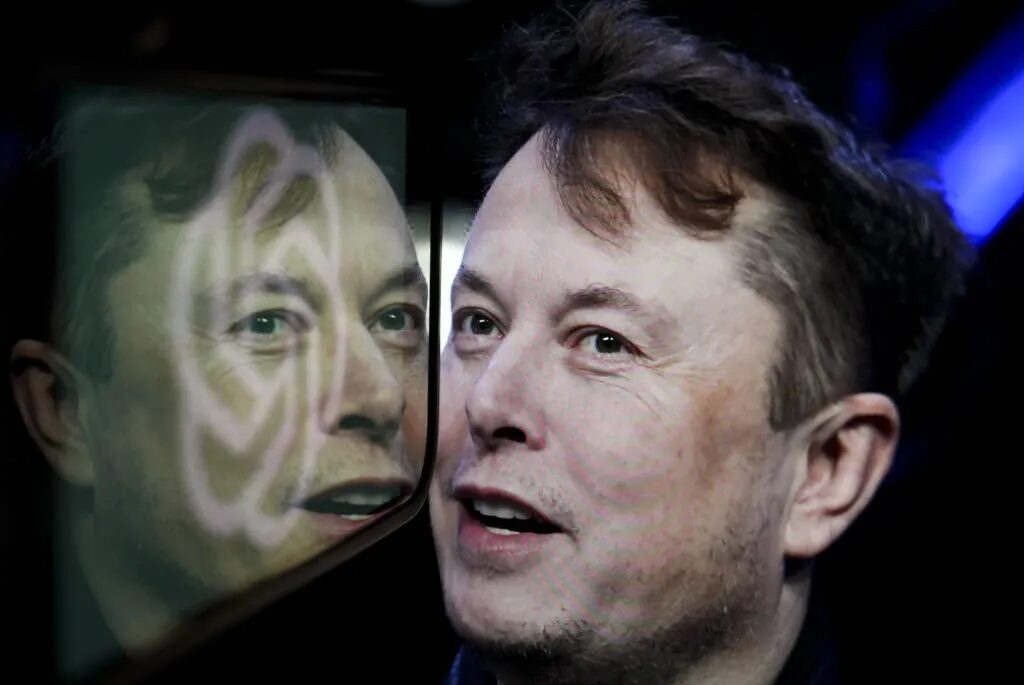 На этой фотоиллюстрации логотип компании «OpenAI» отображается на экране мобильного телефона перед экраном компьютера, на котором размещена фотография Илона Маска.