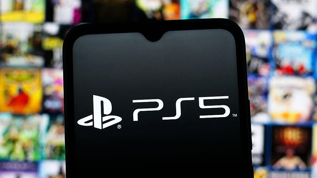 Sony выплатит 7,85 млн долларов в виде подарочных сертификатов для PlayStation Store в рамках урегулирования спора по поводу игровых ваучеров. 1 На переднем плане — телефон с логотипом PlayStation 5, на заднем плане — размытое изображение заставки эксклюзивной игры для PlayStation.