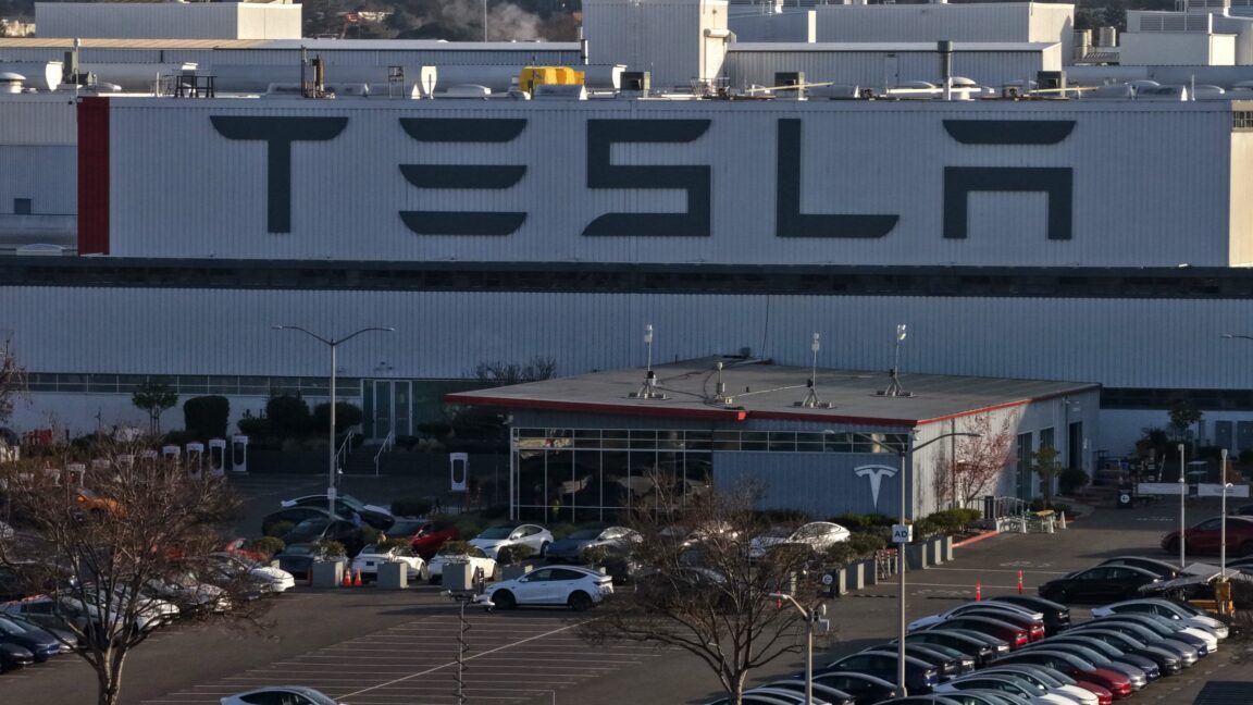 Вид с воздуха на завод Tesla, показывающий парковку и внешний вид здания.