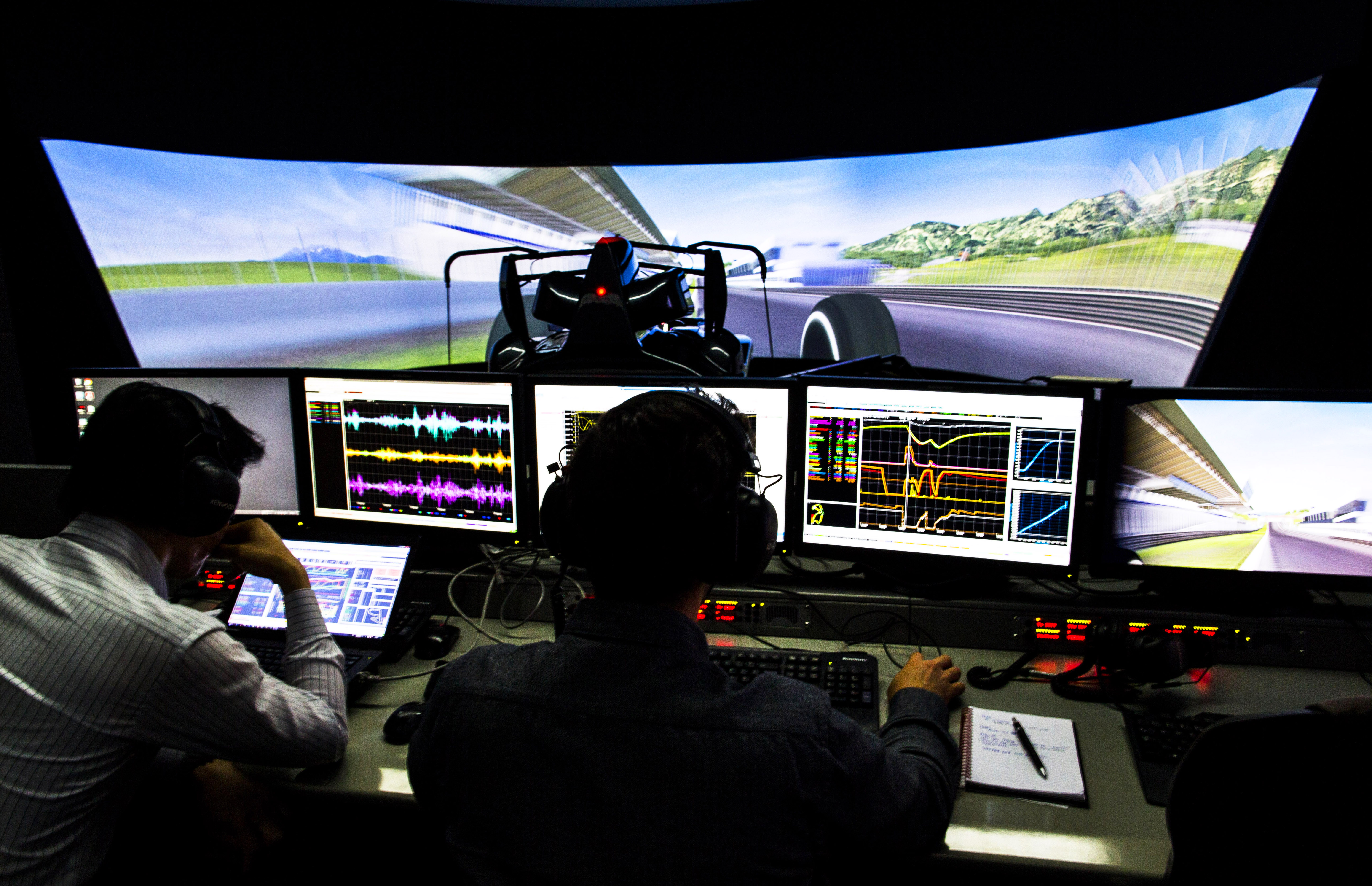 Два технических специалиста McLaren Formula One работают перед компьютерными мониторами, на которых отображаются разноцветные телеметрические данные, полученные с помощью симулятора Формулы-1, за рулем которого находится тест-пилот Формулы-1 (видно по другую сторону экранов). Это произошло в технической зоне McLaren Racing в Техническом центре McLaren в Уокинге, графство Суррей, Великобритания, 23 июня 2016 года. Центр был спроектирован британским архитектором сэром Норманом Фостером, Foster + Partners. (Фото: Даррен Хит/Getty Images)