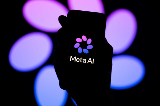 На темном экране смартфона белым цветом написано «Meta AI», а на заднем плане — логотип Meta AI с фиолетовым узором в виде лепестков. Телефон держит темная рука. На заднем плане — увеличенная версия логотипа Meta AI.