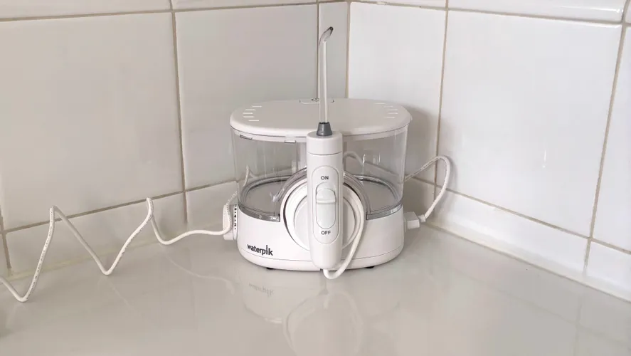 Настольный ирригатор Waterpik Ion на белой столешнице в ванной комнате.