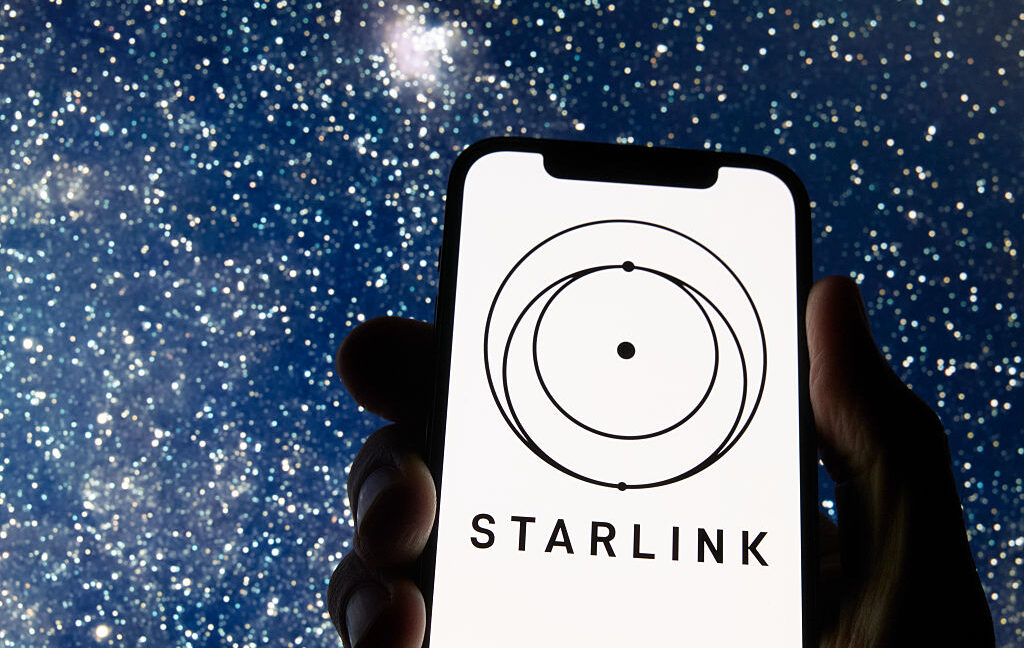 Логотип Starlink появляется на экране смартфона на фоне звездного ночного неба.