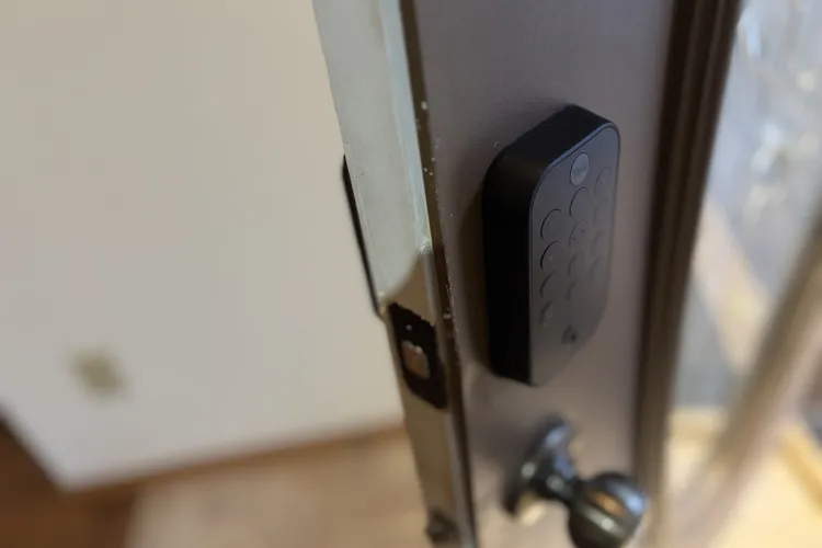 Кодовая клавиатура замка Yale Assure Lock 2 на открытой коричневой двери.