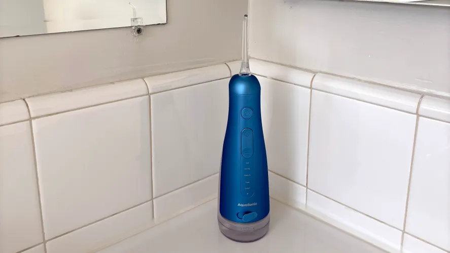 Синий аккумуляторный ирригатор для полости рта AquaSonic Precision на белой столешнице в ванной комнате.