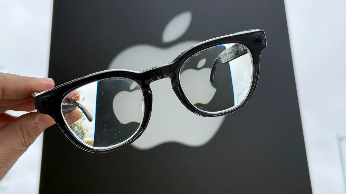 Привет, Siri! Теперь ты — основа для умных очков Apple. 1 Рука, держащая умные очки Meta Ray-Ban на фоне вывески Apple на территории кампуса Apple.