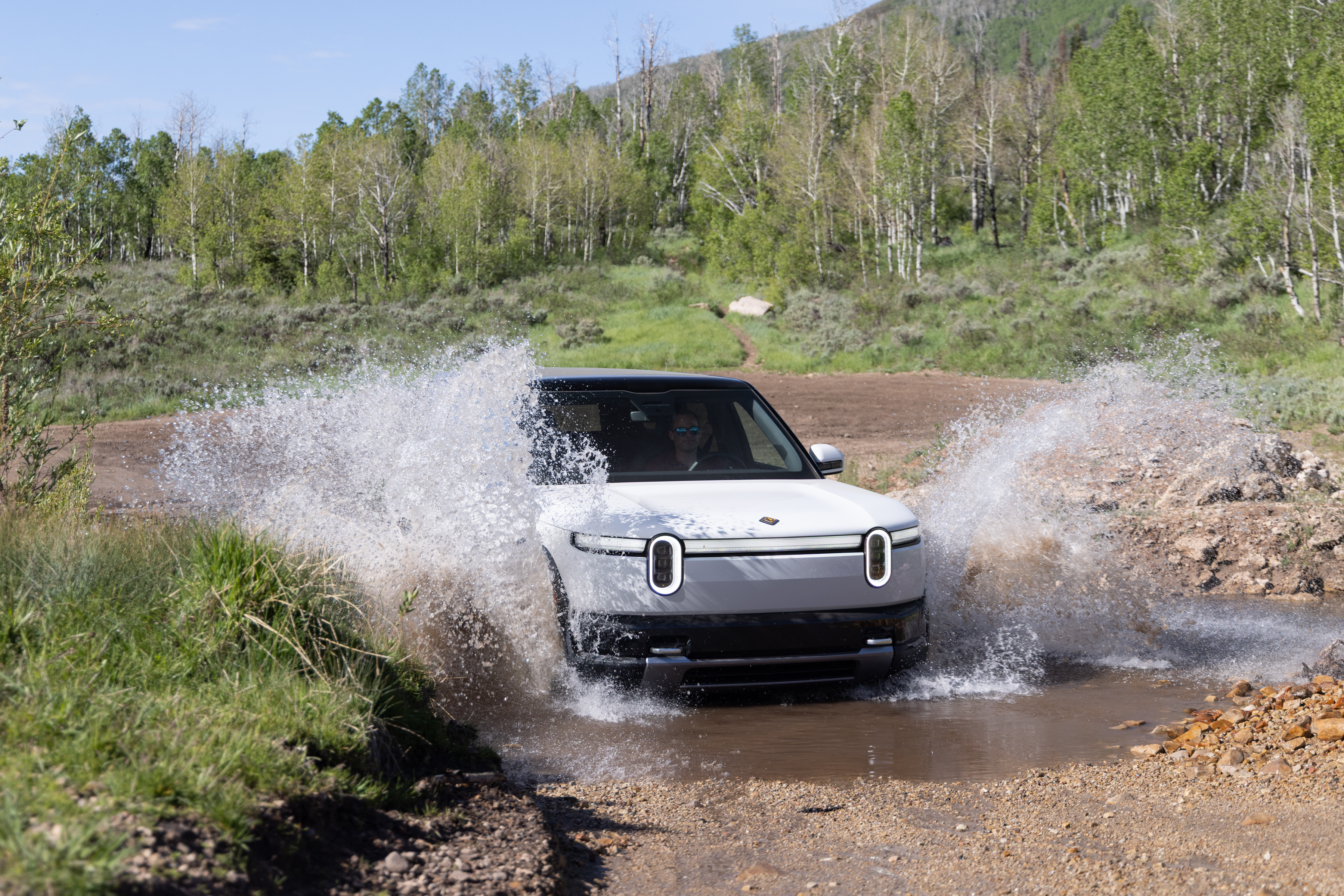 Белый Rivian R2 проезжает сквозь ручей.