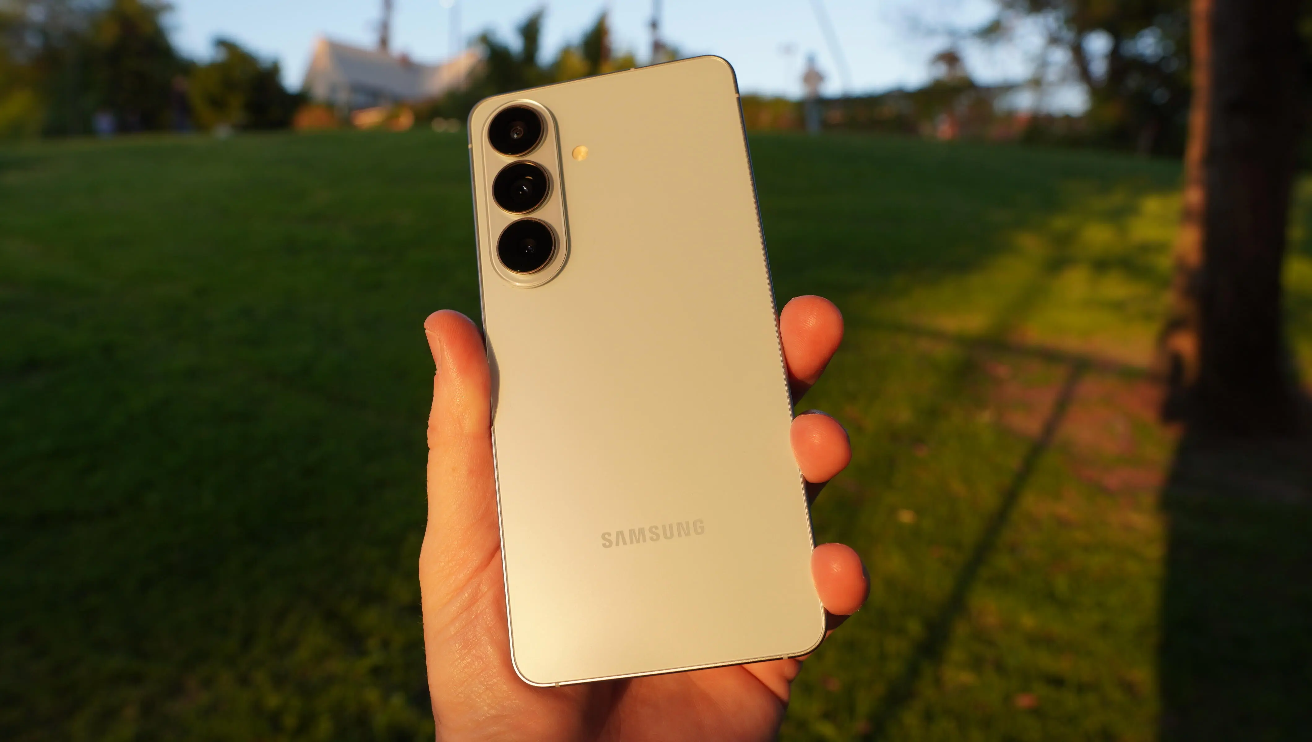 Лучший телефон Samsung 2026 года 13 В парке на закате держали в руках светло-голубой телефон.