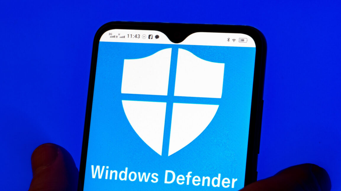 На этой иллюстрации на смартфоне отображается логотип Microsoft Windows Defender, а на заднем плане — логотип Microsoft.