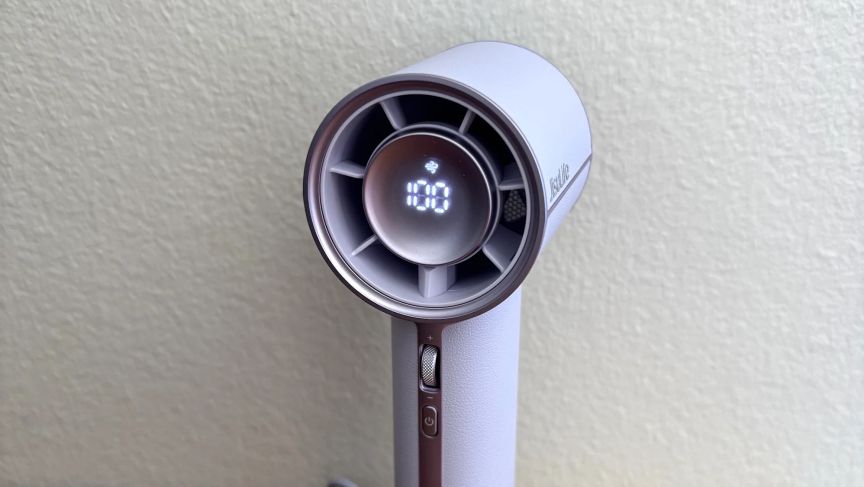 На фоне белой стены стоял ручной вентилятор Jisulife Pro1Mini светло-фиолетового цвета, разогнанный до 100%.