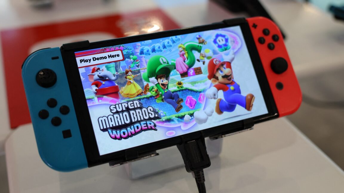 В магазине стоит портативная игровая консоль Nintendo Switch, на экране которой демонстрируется демоверсия игры Super Mario Bros. Wonder.