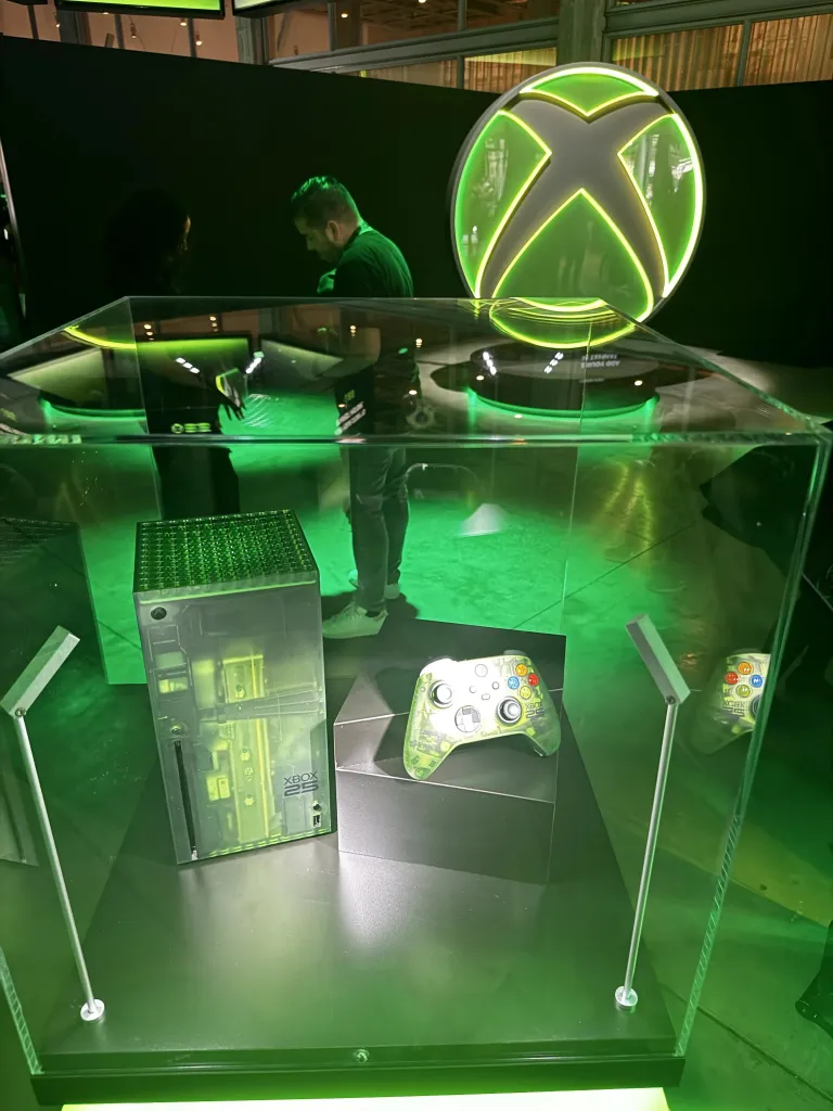 В витрине выставлены Xbox и соответствующий контроллер. Зелёный оттенок подсветки совпадает с зелёным цветом логотипа Xbox.