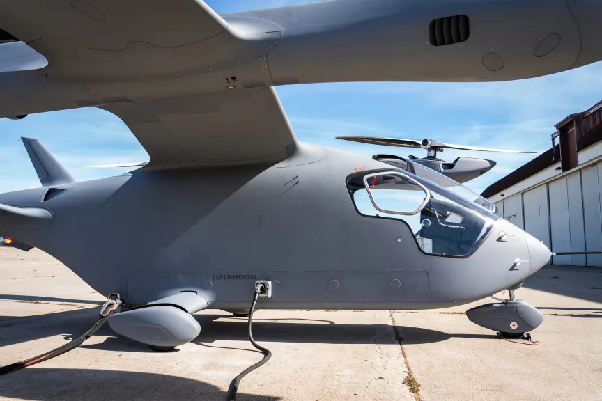 Припаркован летательный аппарат eVTOL. К нему подведены кабели для зарядки.